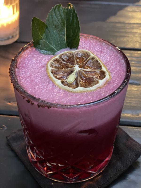 A pink cocktail with citrus and mint beside candlelight