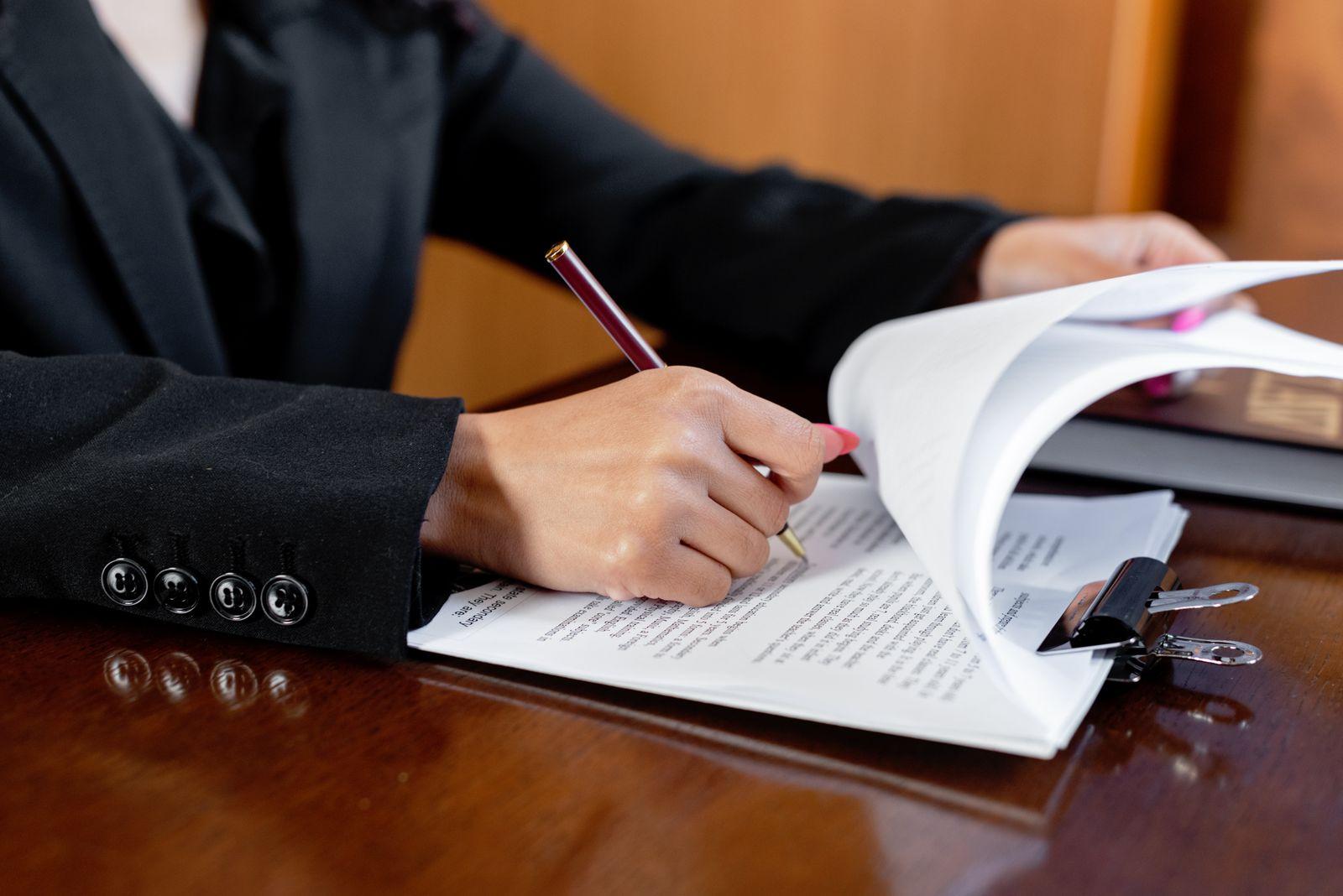 A professional in a dark suit signing legal documents at a wooden office desk