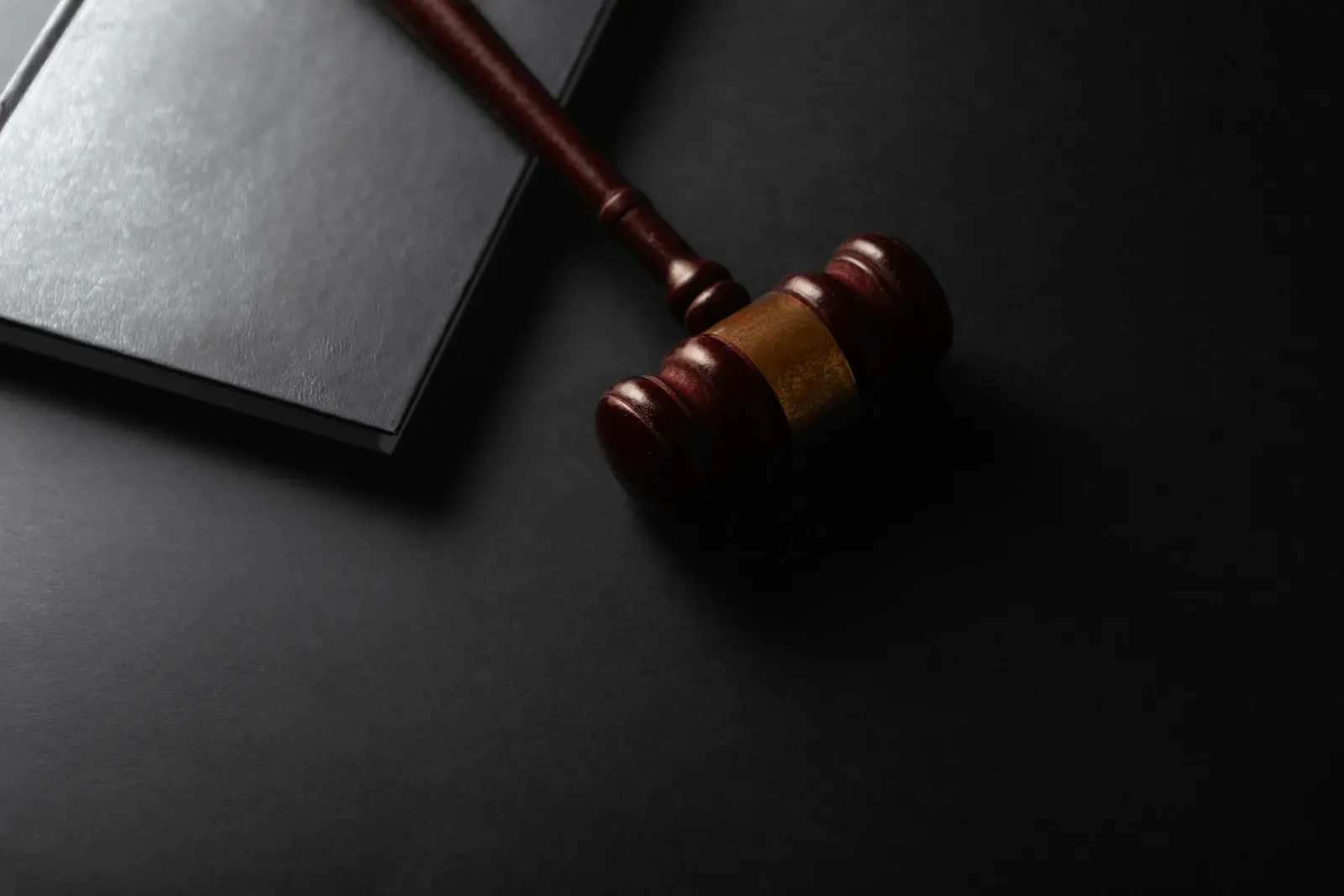 A wooden gavel beside a closed legal book on a dark desk, illustrating a court dispute